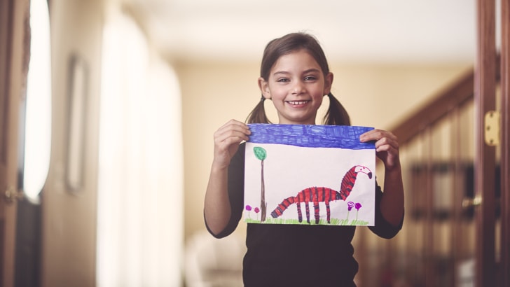 Girl holding up drawing and smiling