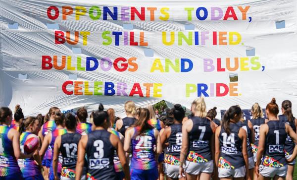 Bulldogs and Blues players run through the Pride banner ahead of an AFLW game