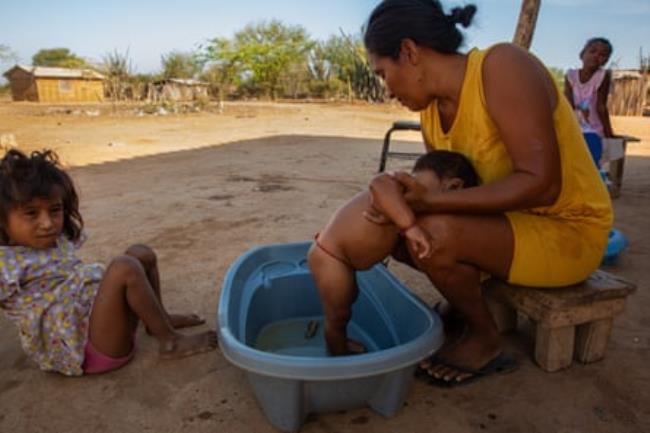 A woman bathes a small boy in a small tub outside while a young girl looks on