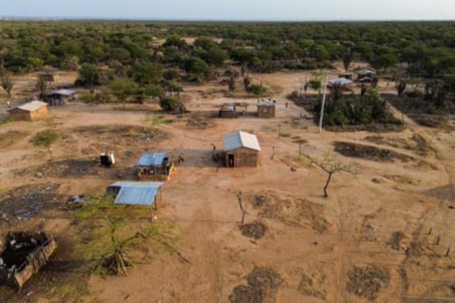 An aerial view of a village with sparse trees and a couple of roughly made wooden houses with tin roofs.