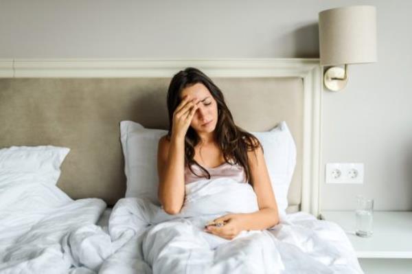 woman lying in bed, feeling unwell, with her hand on her head. Sickness / illness concept. Coro<em></em>navirus / fever / headache concept. Home isolation.