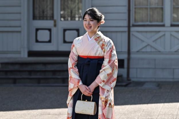 A woman in traditio<em></em>nal Japanese clothing smiles in front of a building