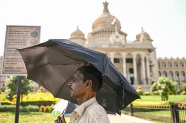 A man takes shelter under an umbrella on a hot summer day near the Vidhana Soudha, State Legislative Assembly, in Bengaluru on April 29, 2024.
