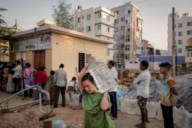 A woman carries a jar of drinking water as people queue at a water vending stall, which extracts and filters borewell water and sells twenty litres of water for five Indian rupees, in Bengaluru, which is facing water shortages, in India, April 25, 2024.