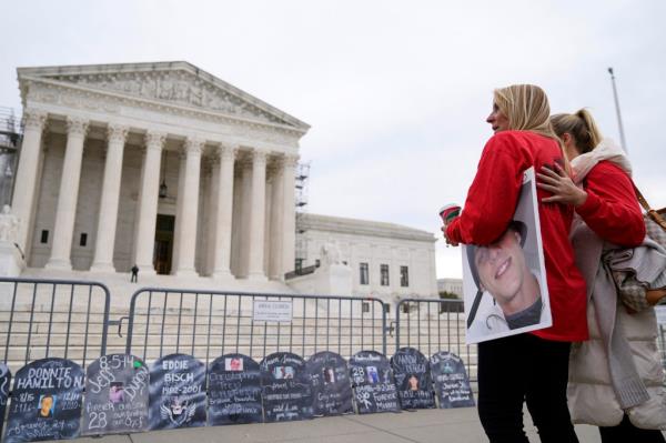 Signs in the shape of grave headstones, with information on people who died from using OxyContin, line a security fence outside the Supreme Court Monday, Dec. 4, 2023, in Washington.