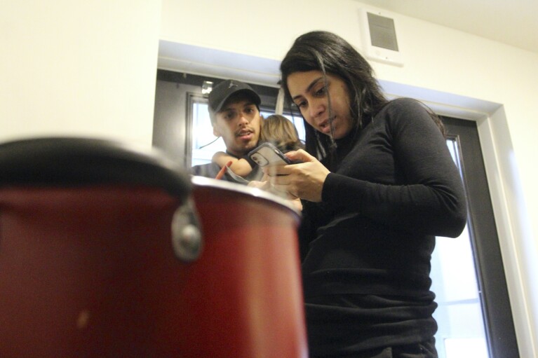 Barbara Peraza-Garcia holds her 2-year-old daughter, Frailys, by the kitchenette section of her 'micro apartment' while her partner, Franklin Peraza, browses Netflix in Seattle on Monday, March 11, 2024. (AP Photo/Manuel Valdes)