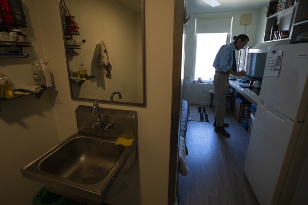 Cheyenne Welbourne is seen standing at his micro-apartment's kitchenette in the Starlight affordable housing building that is run by Central City Concern, a Portland-ba<em></em>sed homeless services nonprofit, on Friday, March 15, 2024, in Portland, Ore. Welbourne moved into one of the nonprofit's single room occupancy units in downtown Portland last March after years of living on the streets. (AP Photo/Jenny Kane)