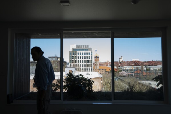 With a view of Portland, Ore., in the background, Cheyenne Welbourne walks in the common room at The Starlight affordable housing building that is run by Central City Concern, a Portland-ba<em></em>sed homeless services nonprofit, on Friday, March 15, 2024. Welbourne moved into one of the nonprofit's single room occupancy units in downtown Portland last March after years of living on the streets. (AP Photo/Jenny Kane)