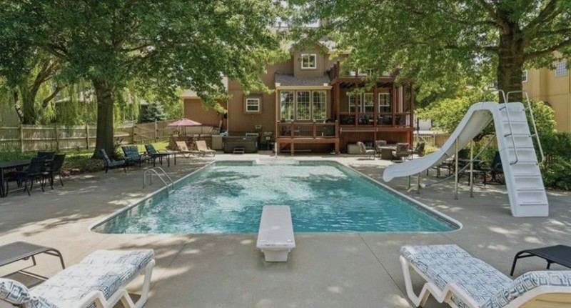 In-ground pool in foreground with two story house in background.