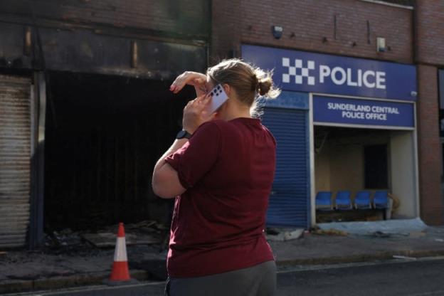 A person uses a cellphone next to a police station damaged by fire.