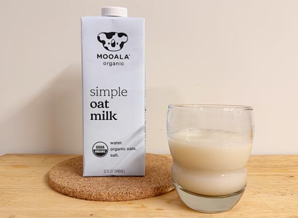 a co<em></em>ntainer of mooala oat milk next to a glass