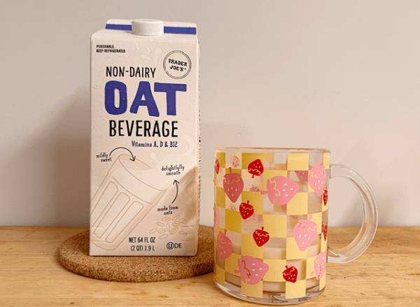 a co<em></em>ntainer of trader joe's oat milk next to a mug with a strawberry print