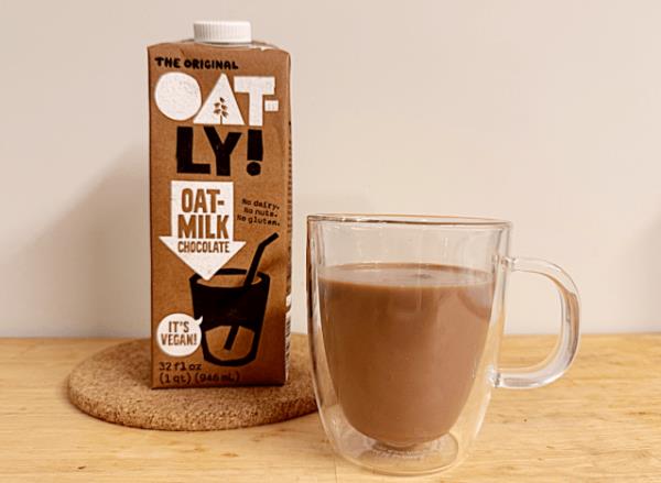 a co<em></em>ntainer of oatly chocolate oat milk next to a coffee mug