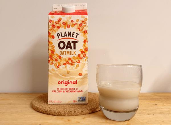 a co<em></em>ntainer of planet oat oat milk next to a glass 