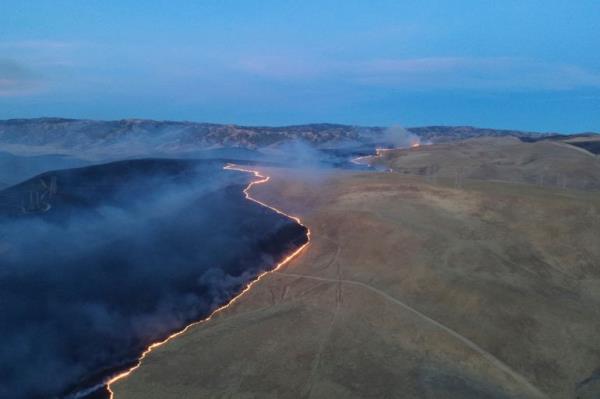 An aerial shot of a wildfire advancing across grassland