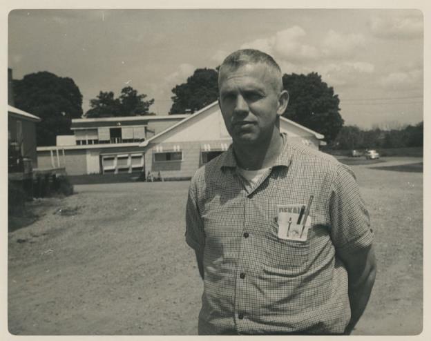 A black-and-white photo of a man standing outside on a farm.