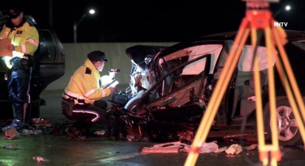 An inestigator shines a flashlight into a crumpled car at the scene. 