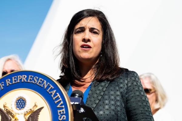 a woman with long black hair speaks from behind a podium