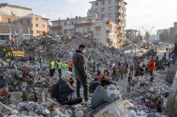 People stand on top of rubble of collapsed buildings during rescue operations in Hatay.