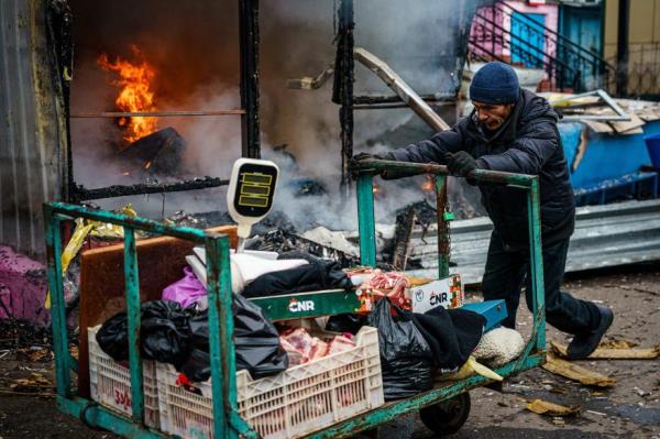 A man pushes a cart in front of a burning shop after Russian shelling to Ukrainian city of Kherson on December 24, 2022, wher<em></em>e five were killed and 20 injured.