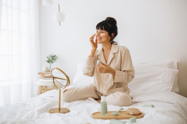 Happy woman doing routine skin care at home with beauty products. 