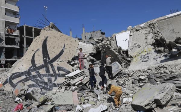 Children stand next to a fallen wall bearing a mural painting amid the rubble of a building destroyed in Israeli bombardment in Rafah in the southern Gaza Strip on February 22, 2024, amid co<em></em>ntinuing battles between Israel and the Palestinian militant group Hamas. (Photo by MOHAMMED ABED / AFP)